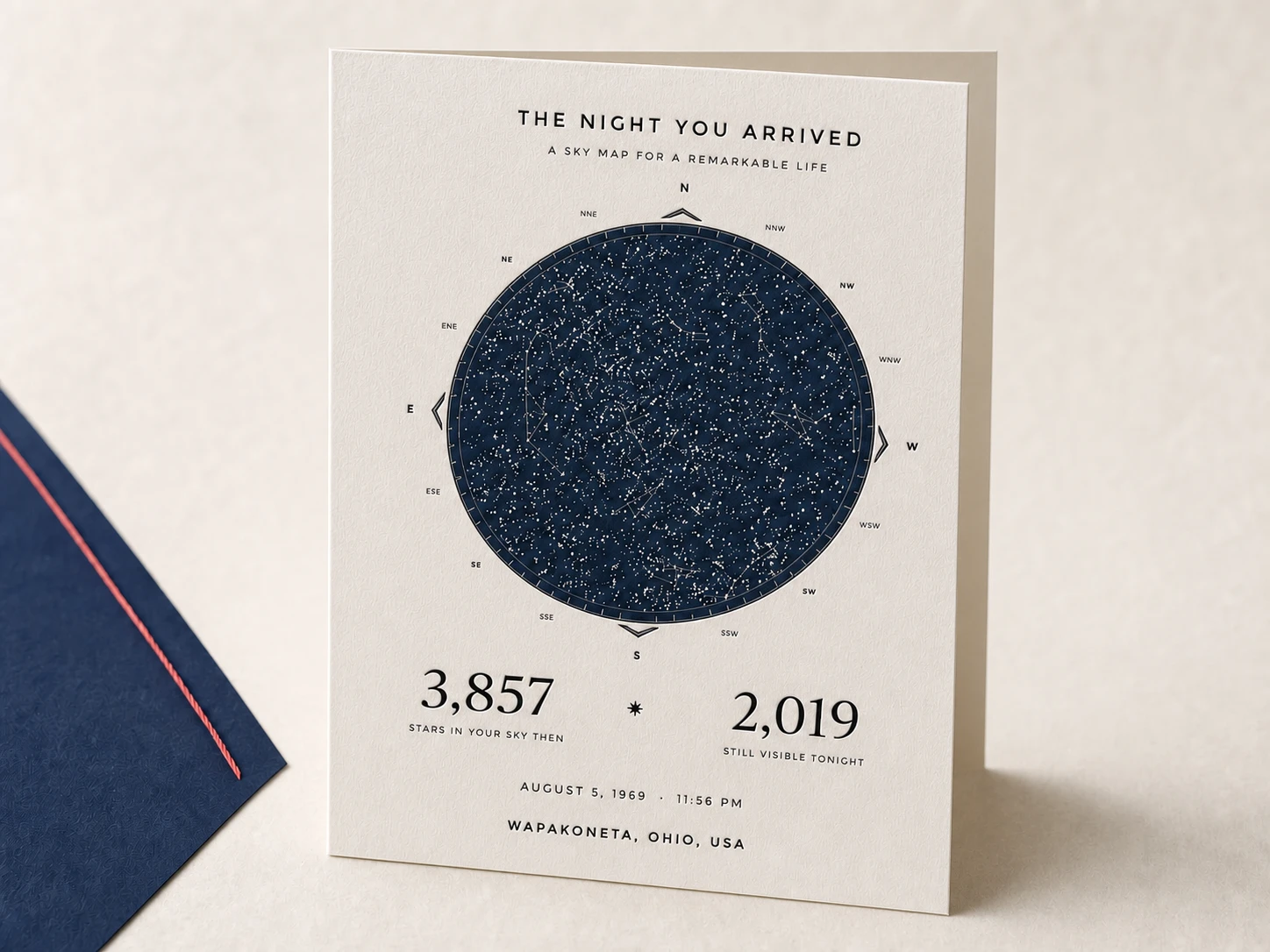 A left-side-fold Illume greeting card standing open like a book beside its navy envelope