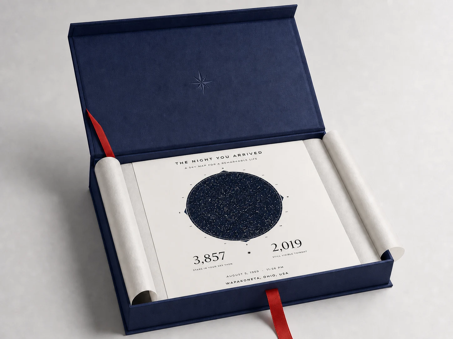 Open navy Illume presentation box with warm-white tissue, red ribbon, and personalized sky map